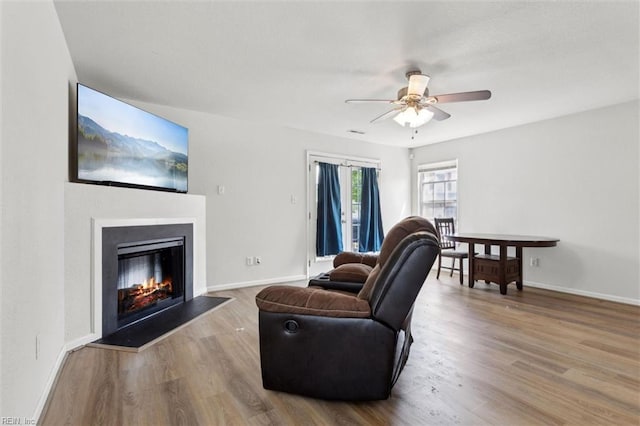 living room with baseboards, a glass covered fireplace, ceiling fan, and wood finished floors