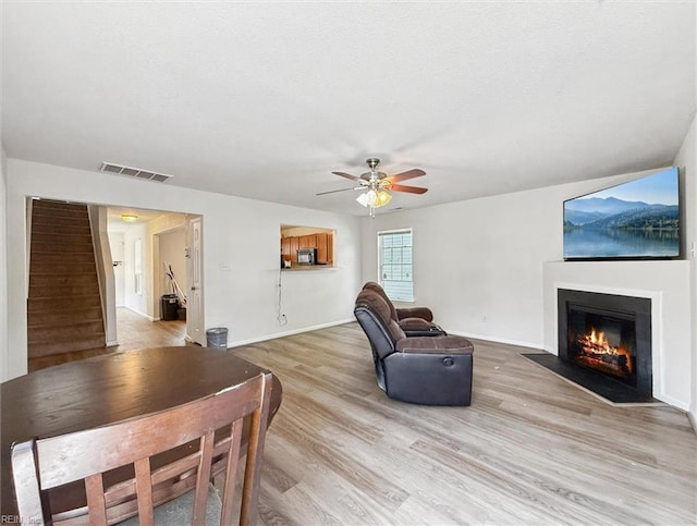 living room featuring ceiling fan, visible vents, a fireplace with flush hearth, light wood-type flooring, and stairs