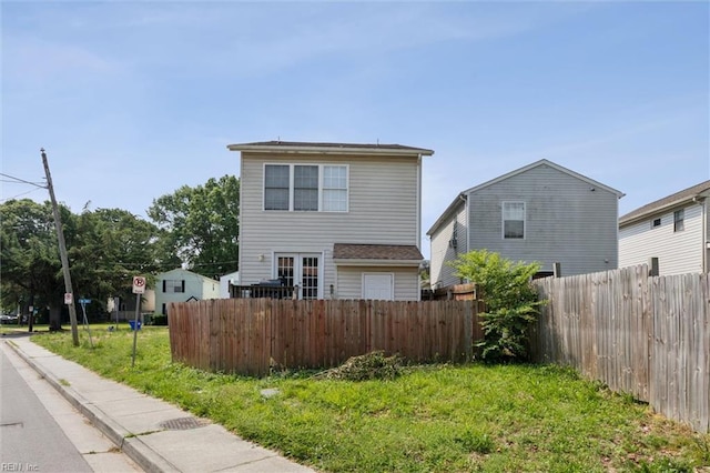 rear view of house with fence, a lawn, and french doors