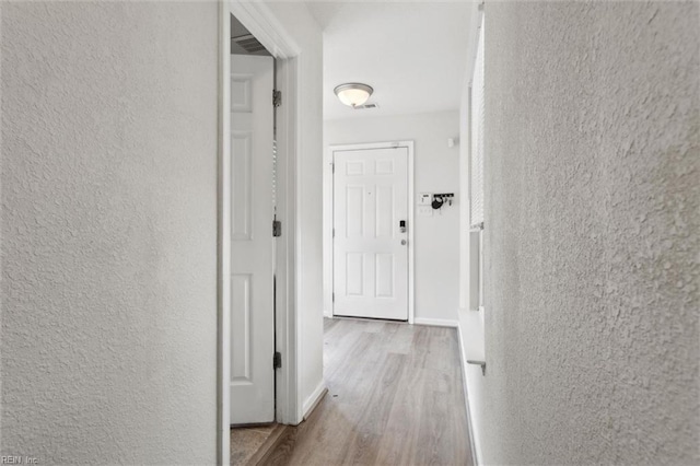 corridor featuring baseboards, a textured wall, and wood finished floors