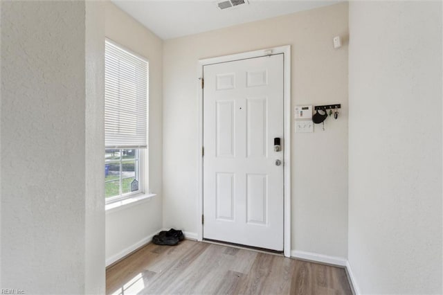 doorway to outside with baseboards, a textured wall, and wood finished floors