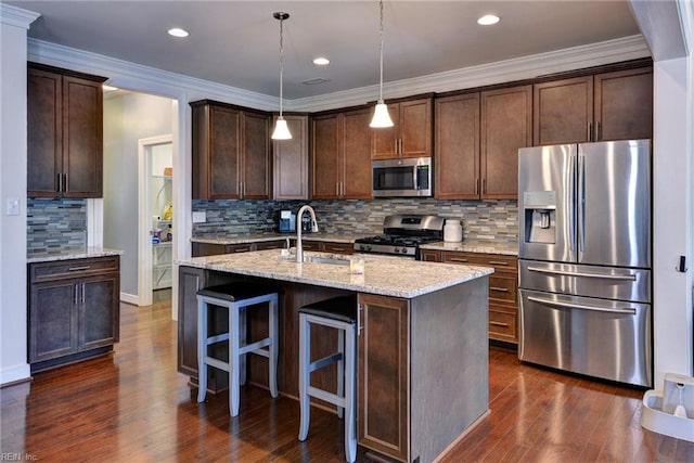 kitchen featuring dark wood-style flooring, dark brown cabinetry, appliances with stainless steel finishes, light stone countertops, and a sink