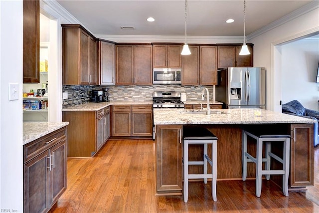 kitchen with a sink, light stone countertops, stainless steel appliances, and light wood finished floors
