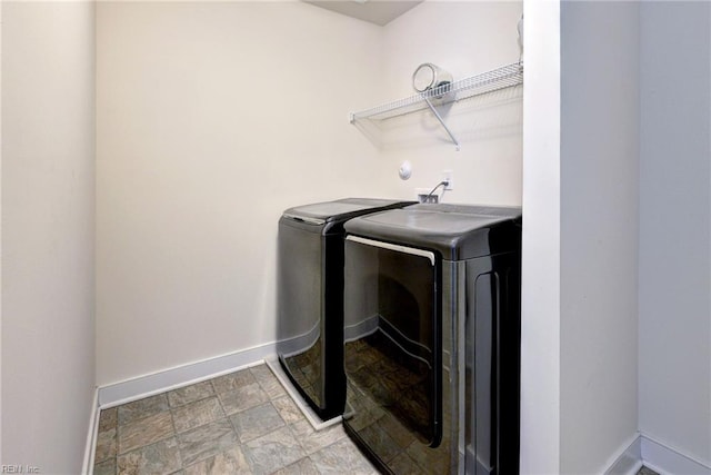 washroom featuring baseboards, laundry area, stone finish floor, and washing machine and clothes dryer