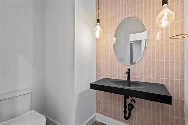 half bath featuring toilet, tile walls, decorative backsplash, and a sink