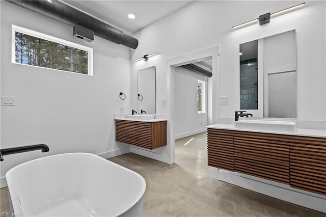 full bath with a soaking tub, concrete floors, a wealth of natural light, and two vanities