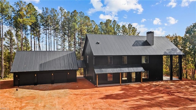 view of front of property with a garage, an outbuilding, metal roof, and a chimney
