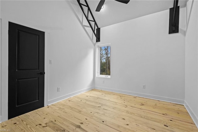 interior space featuring baseboards, light wood-style floors, ceiling fan, and a towering ceiling
