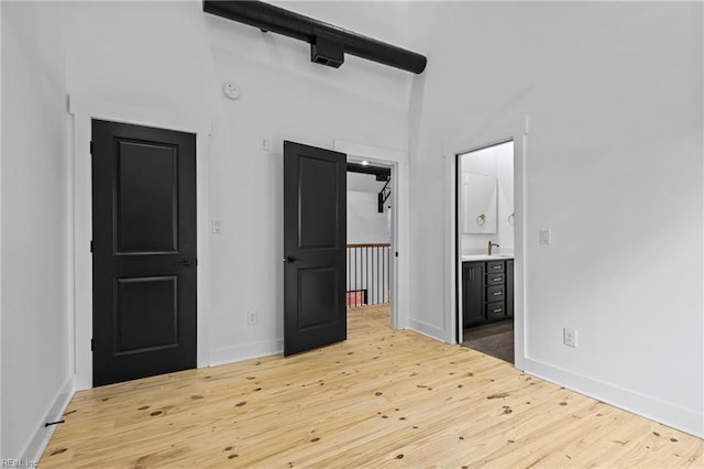 unfurnished bedroom with ensuite bathroom, baseboards, and wood finished floors