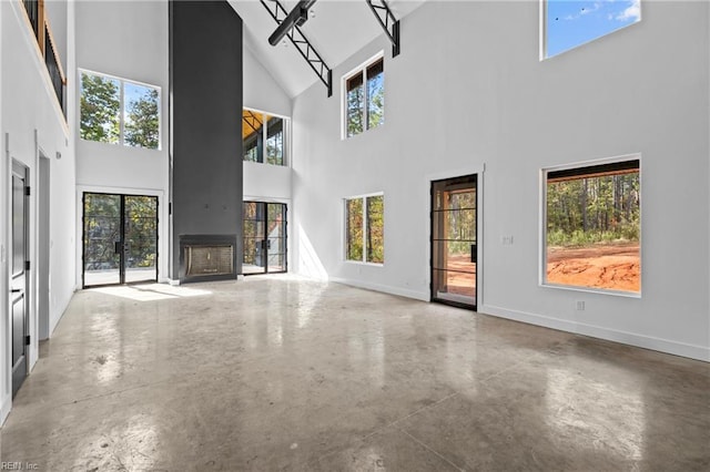 unfurnished living room featuring finished concrete flooring, high vaulted ceiling, baseboards, and a fireplace