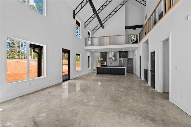 unfurnished living room with baseboards, a sink, a towering ceiling, and concrete flooring