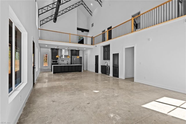unfurnished living room with concrete flooring, baseboards, a sink, and a towering ceiling