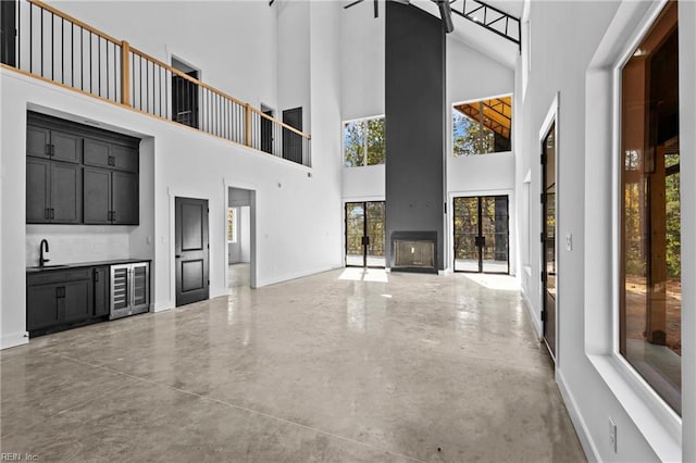 unfurnished living room with wine cooler, baseboards, a high ceiling, a sink, and wet bar