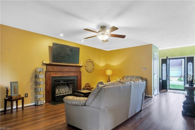 living area featuring wood finished floors, ceiling fan, a fireplace with flush hearth, baseboards, and a textured ceiling