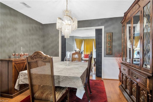 dining space with a chandelier, wood finished floors, and wainscoting