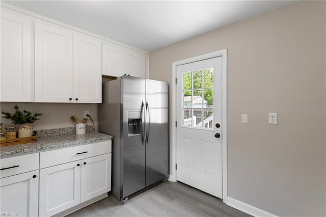 kitchen with white cabinets, light stone counters, light wood-style flooring, baseboards, and stainless steel refrigerator with ice dispenser
