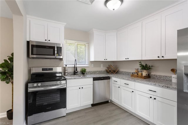 kitchen featuring appliances with stainless steel finishes, a sink, light stone counters, white cabinets, and light wood-style flooring
