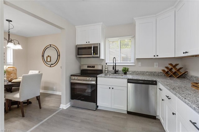 kitchen featuring light stone countertops, a sink, light wood finished floors, stainless steel appliances, and white cabinetry