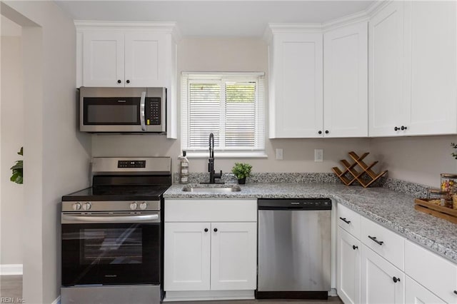 kitchen with a sink, white cabinets, light stone countertops, and stainless steel appliances