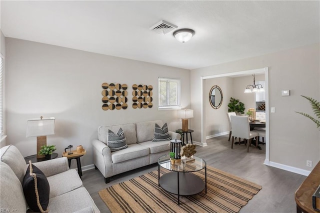 living room featuring visible vents, baseboards, wood finished floors, and an inviting chandelier