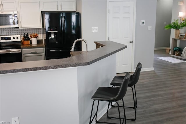 kitchen with a breakfast bar, dark countertops, tasteful backsplash, dark wood finished floors, and stainless steel appliances