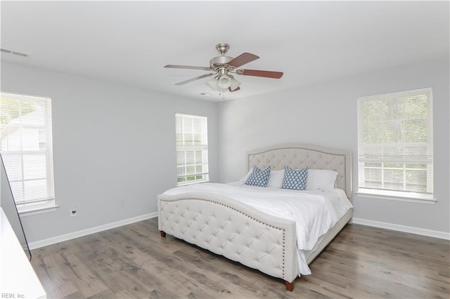 bedroom featuring baseboards, visible vents, multiple windows, and wood finished floors