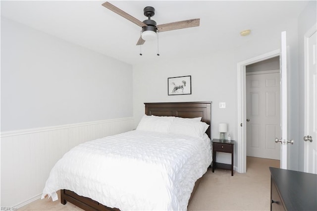 bedroom with wainscoting, ceiling fan, and light carpet