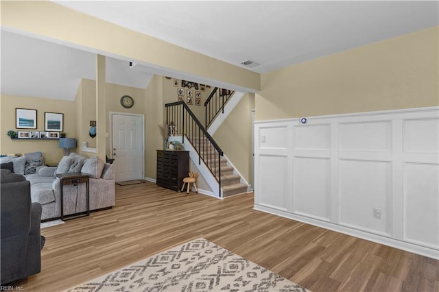 living room featuring visible vents, light wood-style flooring, stairs, and high vaulted ceiling