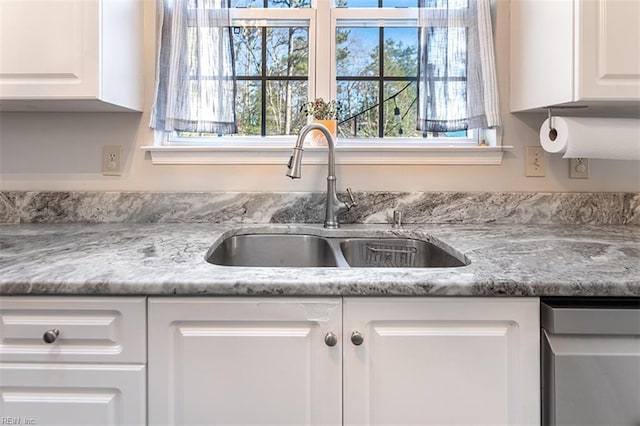 interior details featuring stainless steel dishwasher, white cabinets, and a sink