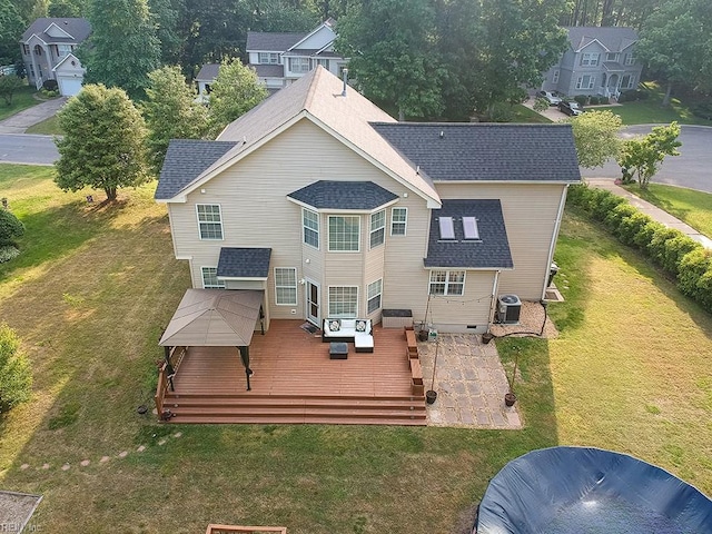 rear view of house with central AC unit, roof with shingles, a wooden deck, and a yard