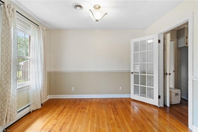 spare room with baseboards, a baseboard heating unit, hardwood / wood-style flooring, and visible vents