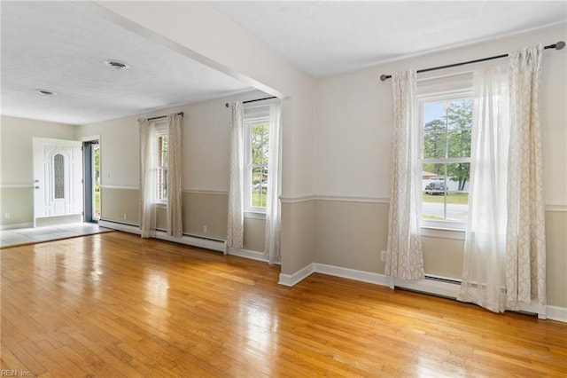 empty room with visible vents, a baseboard radiator, baseboards, and wood finished floors
