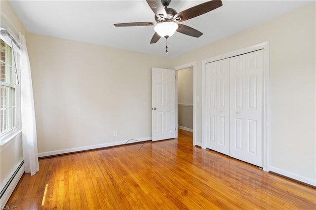 unfurnished bedroom featuring light wood-type flooring, a baseboard radiator, a closet, and multiple windows