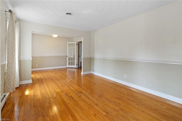 unfurnished room with a baseboard heating unit, baseboards, visible vents, and light wood finished floors