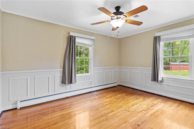 empty room with wainscoting, ornamental molding, a baseboard heating unit, and wood finished floors