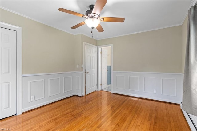 unfurnished bedroom featuring wood-type flooring, ceiling fan, wainscoting, and ornamental molding
