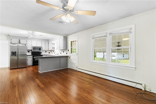 kitchen featuring appliances with stainless steel finishes, baseboard heating, a sink, a peninsula, and dark wood-type flooring