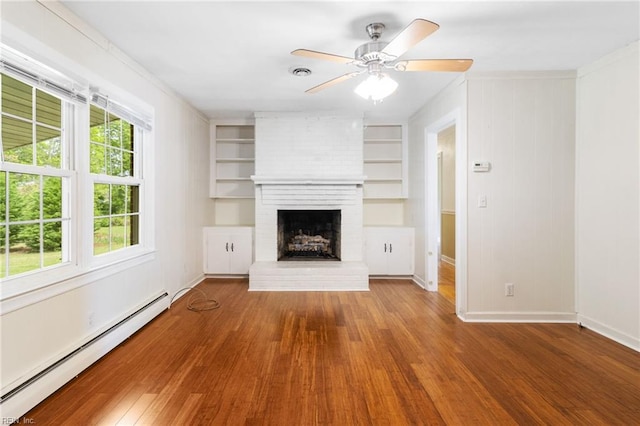 unfurnished living room with a brick fireplace, baseboards, a baseboard heating unit, and wood finished floors