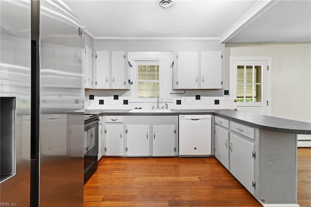 kitchen featuring white dishwasher, dark countertops, stainless steel fridge, a sink, and black range with electric cooktop