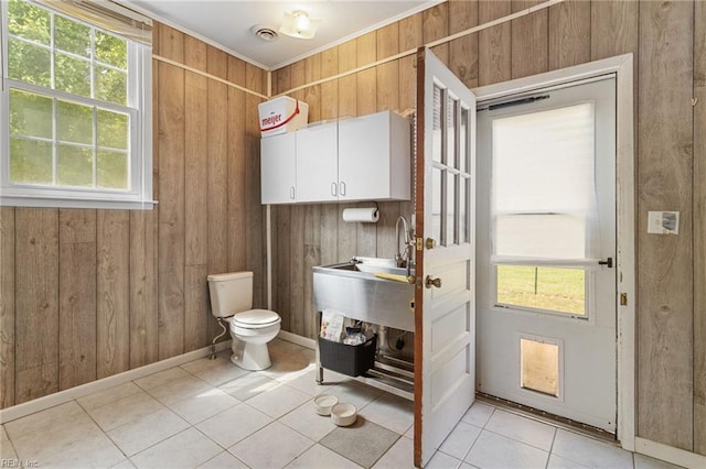half bathroom with wooden walls, crown molding, toilet, tile patterned floors, and visible vents