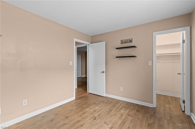 unfurnished bedroom featuring wood finished floors, a spacious closet, baseboards, and a closet