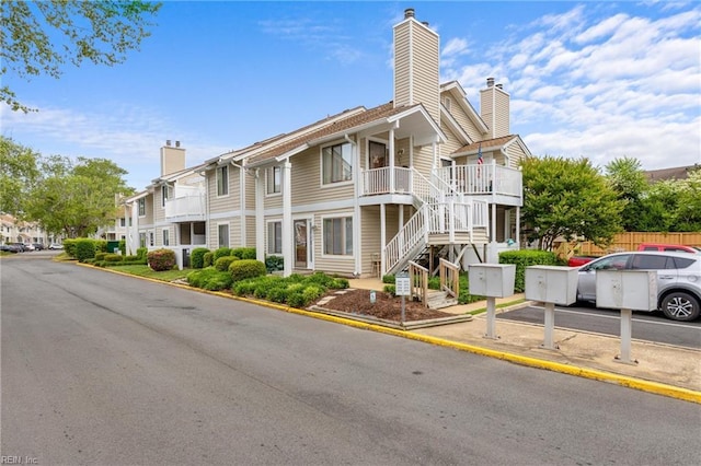 view of building exterior featuring uncovered parking, stairs, a residential view, and fence