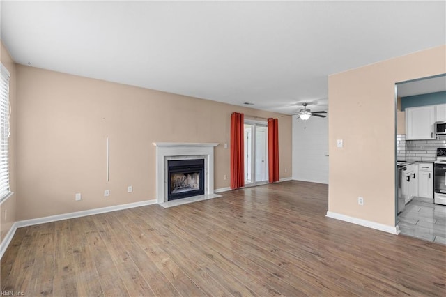 unfurnished living room with light wood-style floors, a ceiling fan, a fireplace, and baseboards