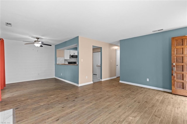 unfurnished living room with wood finished floors, ceiling fan, baseboards, and a sink