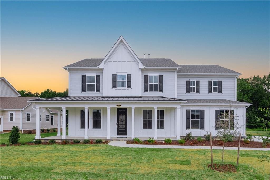 modern farmhouse featuring a standing seam roof, covered porch, board and batten siding, and a front lawn