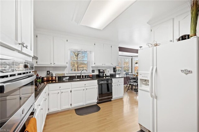 kitchen featuring a sink, white refrigerator with ice dispenser, black dishwasher, and white cabinetry