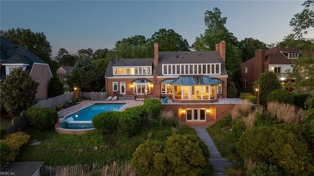 rear view of house featuring french doors, a chimney, a patio area, a fenced in pool, and a fenced backyard