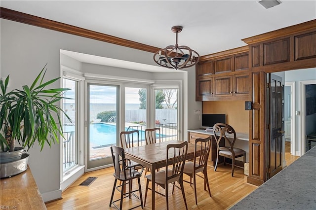 dining space featuring visible vents, light wood finished floors, crown molding, and a notable chandelier