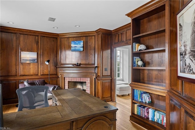 office featuring a brick fireplace, wooden walls, recessed lighting, and light wood finished floors
