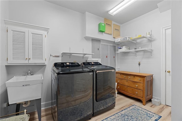 clothes washing area featuring a sink, washing machine and dryer, light wood-style flooring, and electric panel